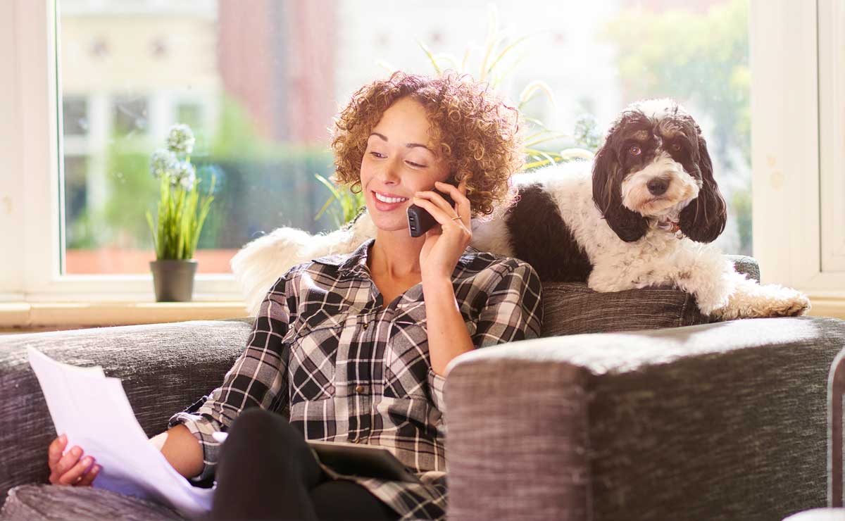 Photo of woman on phone with dog beside her representative of pet health insurance market.